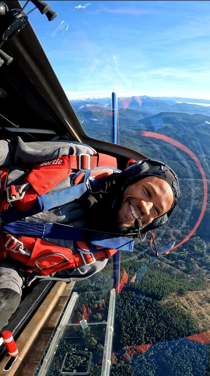 Doug Byrd inverted in the cockpit, a snow-capped range on the horizon and a forested valley below.