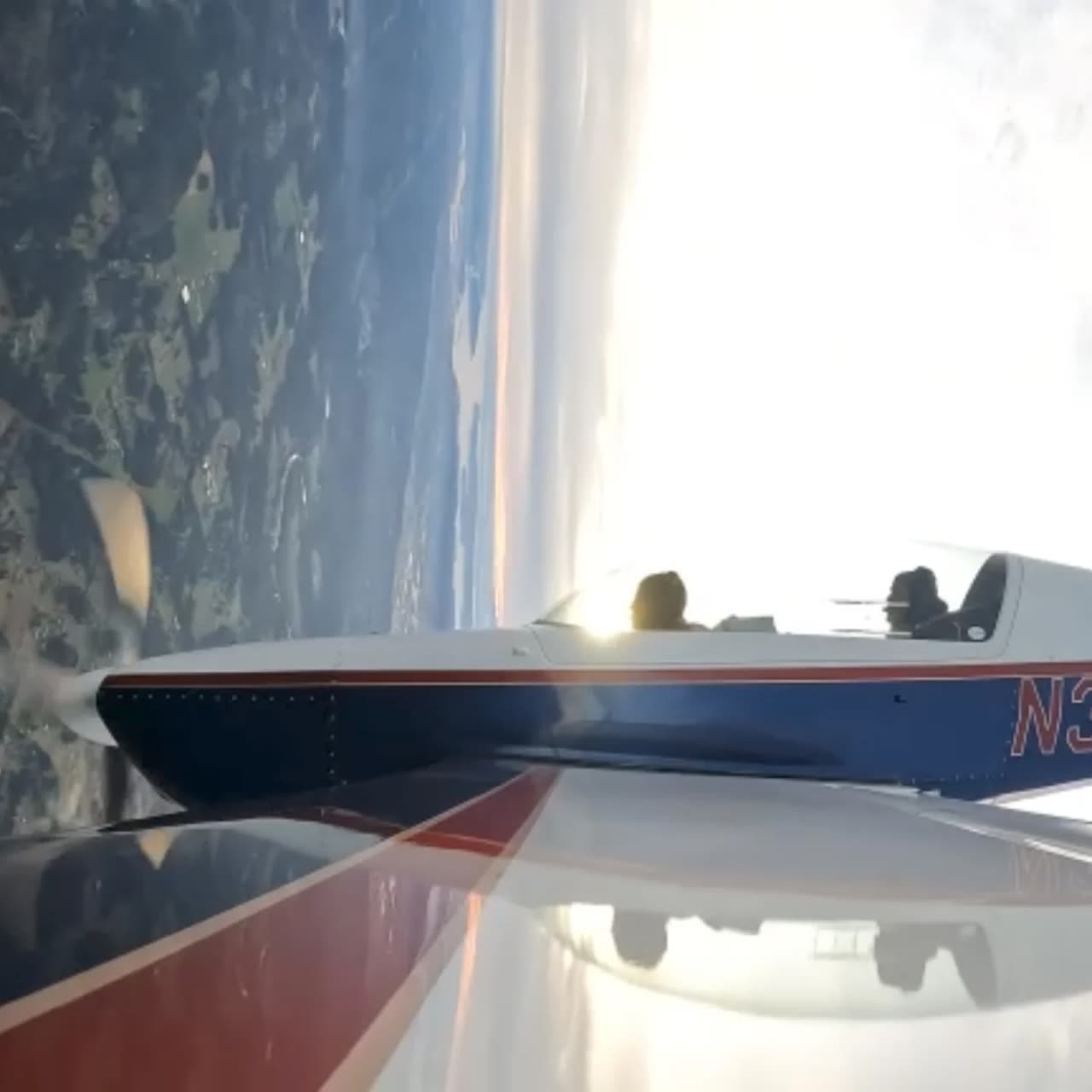 An Extra 300L in a steep bank over water and forest at golden hour, seen past the wing of the camera ship.