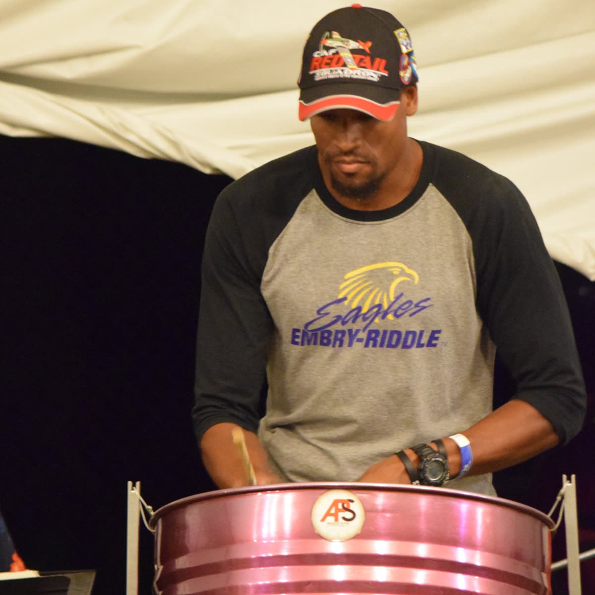 Doug Byrd playing steel pan at EAA AirVenture, wearing a CAF Red Tail cap